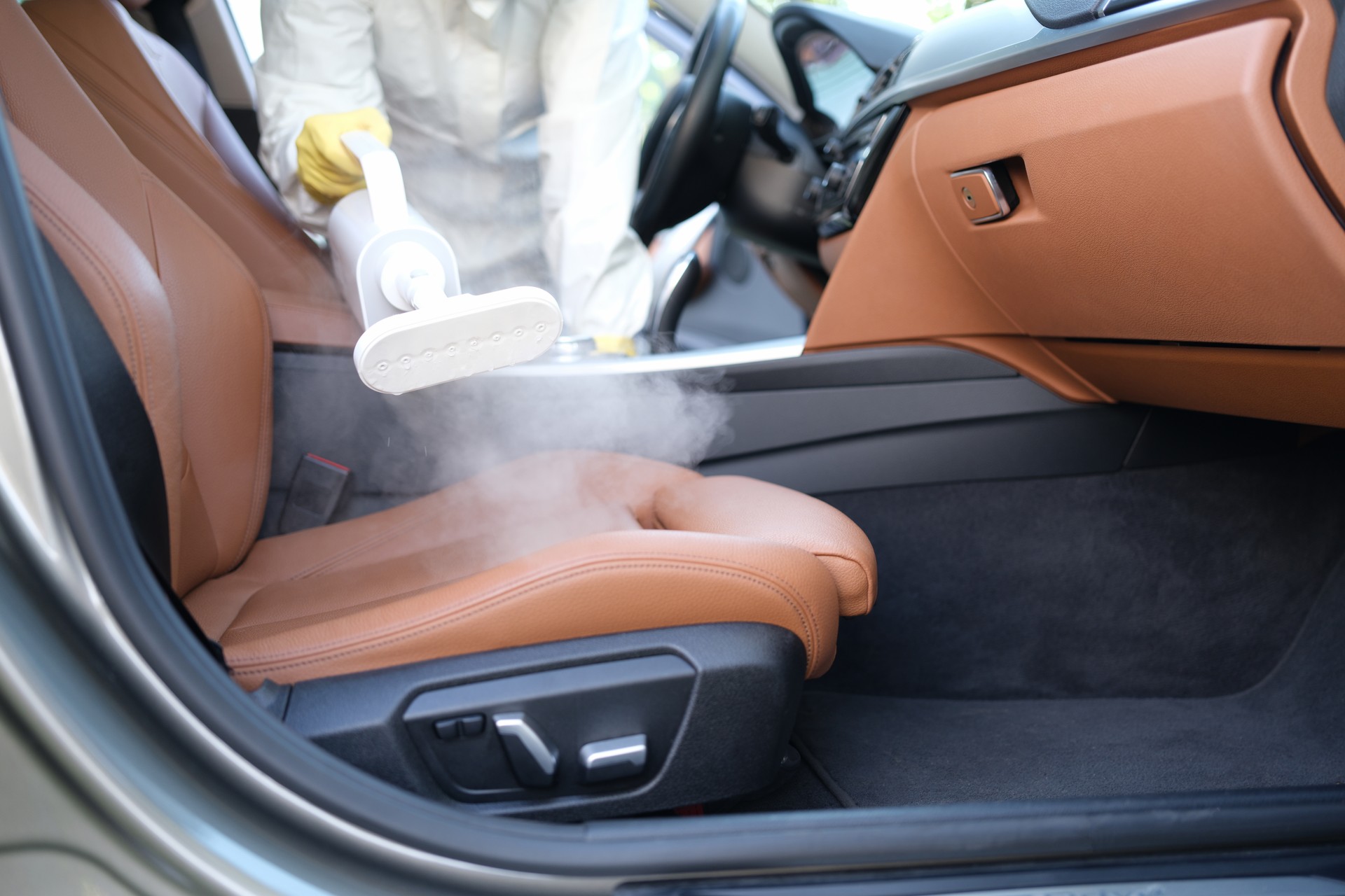 Man in protective suit cleaning car interior with steamer closeup